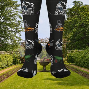 May include: Black socks with a repeating pattern of lawn care equipment and a person on a riding mower. The design includes a lawn mower, rake, wheelbarrow, and other gardening tools. The socks are knee-high.