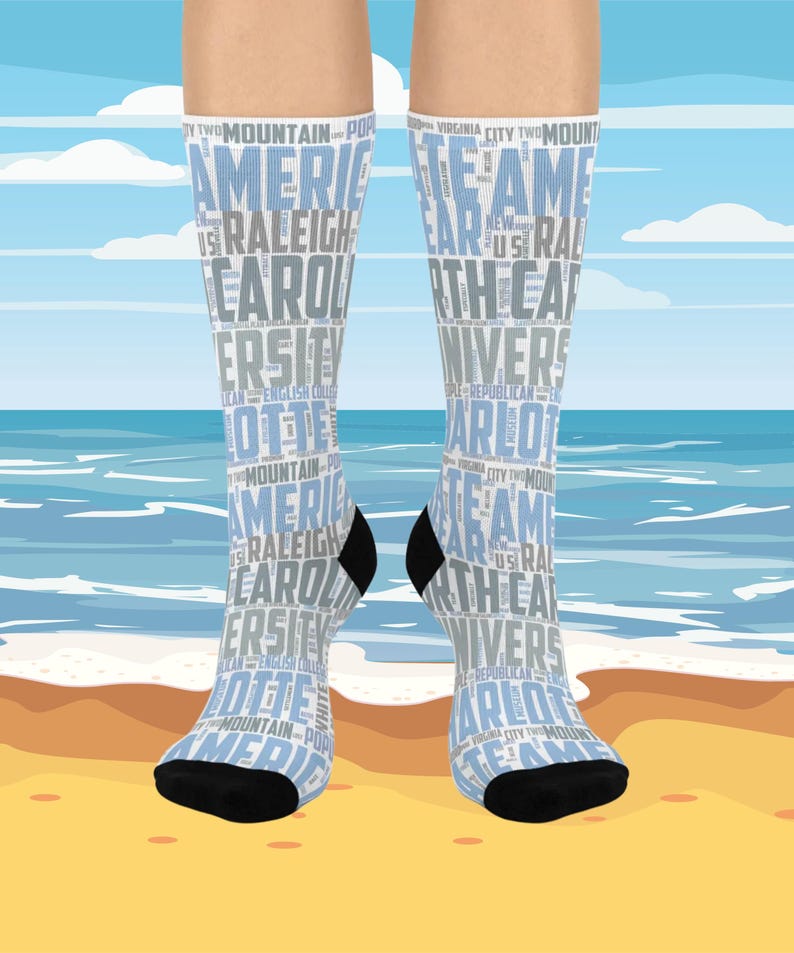 May include: A pair of knee-high socks with a light blue and white design. The socks feature text including "America", "Raleigh", "Carolina", and "University". The toes and heels are black. The background shows a beach scene.