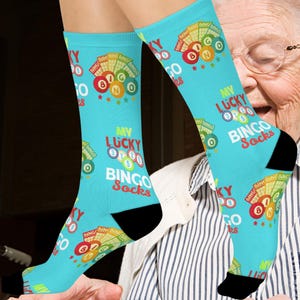 May include: Light blue socks with the text "MY LUCKY BINGO Socks" and bingo ball graphics. The socks have black heels and toes. The design includes the numbers 0, 7, and 8, along with stars and the word "BINGO".