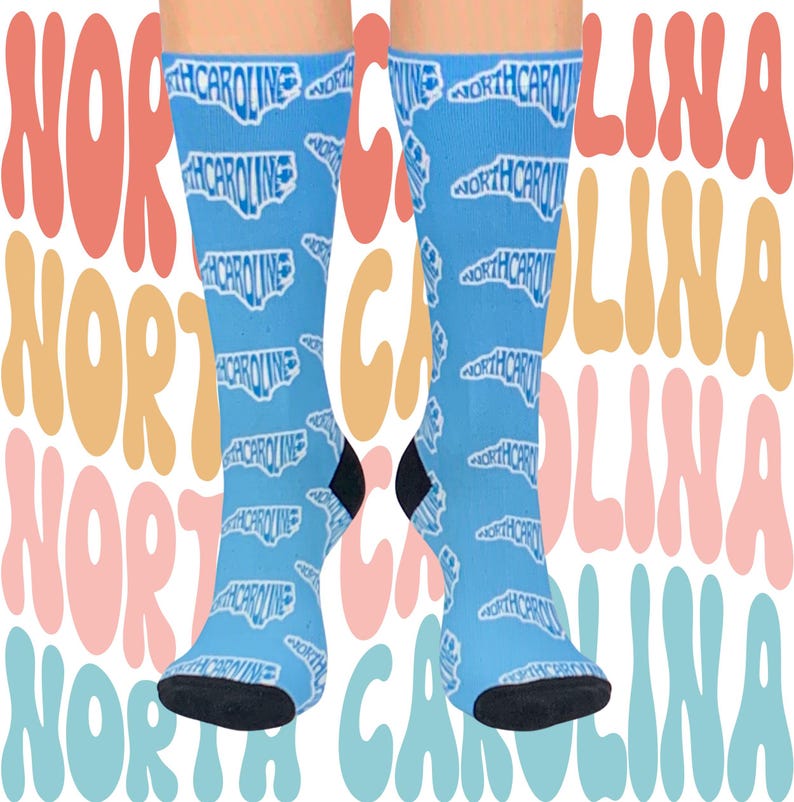 May include: A pair of blue socks with a white outline of the state of North Carolina repeated on the fabric. The socks are on a background of colorful text that says "North Carolina".