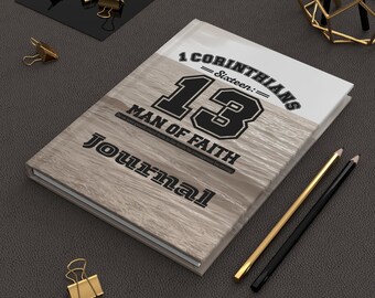 May include: A journal with a light wood grain cover featuring the text "1 Corinthians 13" and "Man of Faith." The journal is accompanied by gold and black pencils, and gold binder clips. The journal's title is "Journal."