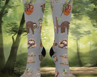 May include: Gray knee-high socks with a repeating pattern of sloths in various poses. The sloths are brown, tan, and orange, with green tree branches. The socks have black heels and toes.