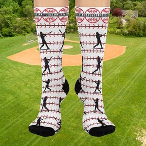 Könnte beinhalten: Weiße Baseballsocken mit einem sich wiederholenden Muster aus roten Baseballnähten und Silhouetten von Baseballspielern. Auf der Oberseite der Socken befindet sich das Wort "BASEBALL" in einem sich wiederholenden Muster. Die Socken haben schwarze Fersen und Zehen.