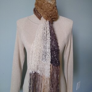 May include: A brown, white, and purple knit scarf with fringe. The scarf is draped over a mannequin wearing a beige sweater.