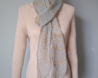 Peut inclure: Une écharpe bleu clair et or avec un motif en tricot délicat et des franges. L'écharpe est drapé autour du cou d'un mannequin.