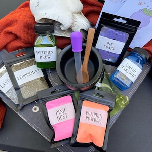 May include: A collection of witch-themed items, including a small black cauldron, a bottle labeled "Witches Brew," and packets of "Peppermint," "Pixie Dust," and "Pumpkin Powder." Also included are "Mini Soaps" and a bottle of "Liquid Starlight."