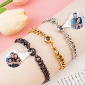 May include: Three stainless steel chain bracelets with a small round charm that projects an image when viewed from a specific angle. The charms are black, gold, and silver.