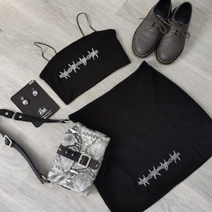 Può includere: Set di top corto e gonna neri con un design a filo spinato. Il set include una borsa a tracolla in pelle di serpente nera e un paio di scarpe grigie con lacci.