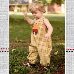 May include: A toddler wearing a yellow and brown checked bubble romper with a pumpkin patch appliqué. The romper has a bib style top and a gathered bottom. The toddler is standing in a grassy area. The image is titled "Huxley's Bubble Romper" and has a polka dot umbrella graphic at the top.