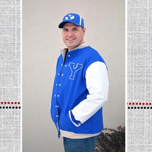 Op de afbeelding: Een blauwe varsity-jas met witte mouwen en een grote witte "Y" op de borst. De jas wordt gedragen door een persoon die een blauw-witte baseballcap draagt. De tekst "Polka Dot Umbrella" en "Brock's Letterman Jacket" zijn ook zichtbaar.