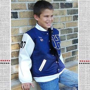 Puede incluir: Una chaqueta de béisbol azul y blanca con una manga blanca y una manga azul. La chaqueta tiene una franja blanca en la parte delantera y un cuello blanco. La chaqueta tiene una letra blanca "H" en el lado derecho del pecho y el número "07" en el lado izquierdo del pecho. La chaqueta tiene un pequeño parche con la palabra "Edgar" en él. La chaqueta la lleva un niño pequeño que sonríe. Chaqueta de béisbol de Brock.