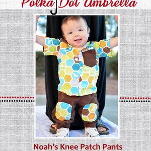 Könnte beinhalten: Ein Kleinkind trägt ein braunes und blaues gemustertes Hemd und eine braune Hose mit bunten Knie-Patches. Die Hose hat ein Wabenmuster. Das Kleinkind steht auf einer weißen Oberfläche. Das Bild ist mit "Noah's Knee Patch Pants" betitelt.