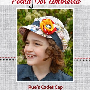 May include: A white cadet cap with a colorful flower embellishment and a blue ribbon. The cap has a printed design with a polka dot pattern. The text "Rue's Cadet Cap" is printed below the image.