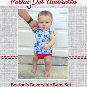 May include: A baby boy wearing a blue and white reversible baby set with a red and white polka dot pattern on the reverse side. The set features a sleeveless top and a diaper cover. The baby is standing and holding the hand of an adult. The text "Boston's Reversible Baby Set" is at the bottom of the image.
