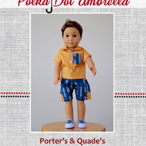 May include: A doll wearing a yellow and orange patterned short-sleeved shirt with a blue and white patterned pocket and blue and white patterned shorts. The doll is standing on a wooden surface. The text "Polka Dot Umbrella" is at the top of the image and the text "Porter's & Quade's" is at the bottom of the image.