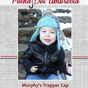 May include: A blue and white polka dot trapper hat with ear flaps. The hat is made of soft, fuzzy fabric and has a black leather patch with the text "Next Ames 1985 Club".