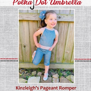 May include: A little girl wearing a blue denim romper with a pink waistband. She is standing in front of a wooden fence and smiling. The text "Kinzleigh's Pageant Romper" is at the bottom of the image.