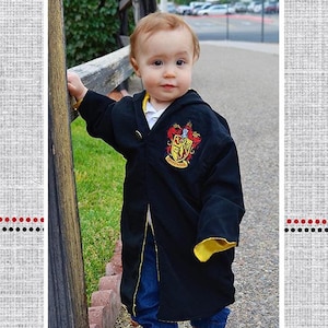 May include: A young child wearing a black robe with a yellow lining and a Gryffindor crest embroidered on the front. The robe is called "Malcolm's Character Robe" and is part of a collection called "Polka Dot Umbrella".