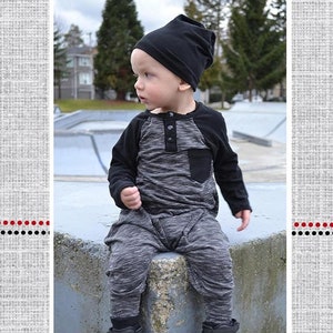 May include: A baby boy wearing a gray and black raglan romper with a black beanie. The romper has a pocket on the front and a button closure at the neck. The text "Mason's Raglan Harem Romper" is at the bottom of the image.