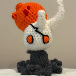 Può includere: Bambola all'uncinetto fatta a mano con testa bianca, occhi arancioni e design a crepa nera. Ha un copricapo arancione e rosso e una base grigio scuro con un design a tentacoli. Un oggetto unico fatto a mano.