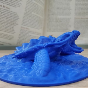 May include: A blue 3D printed miniature of a dragon turtle, with the dragon's head open in a roar, on a blue base.