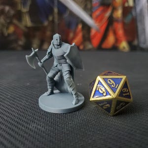 May include: A gray plastic miniature figure of a knight holding a battle axe and a shield. The figure is standing on a round base. A blue and gold dice is in the background.