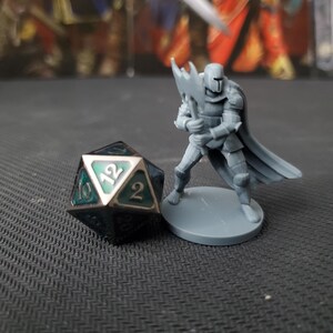 May include: A gray plastic miniature of a knight holding a battle axe, standing on a gray base. A green and silver 12-sided die is in the foreground.