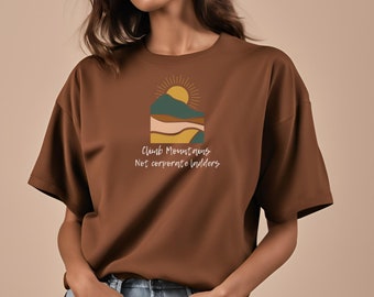 Puede incluir: Una camiseta marrón con un gráfico de una cordillera con un sol saliendo detrás. El texto "Climb Mountains Not Corporate Ladders" está impreso debajo del gráfico.