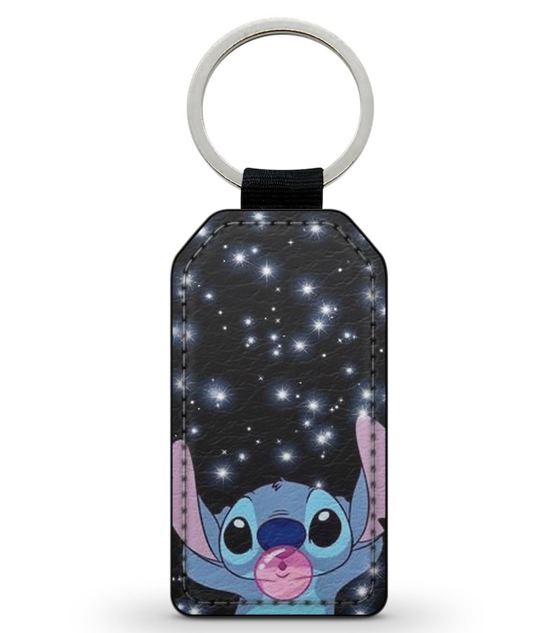 May include: A blue Stitch character from Lilo & Stitch is holding a pink bubble with a starry night background. The keychain is made of black faux leather with a silver key ring.