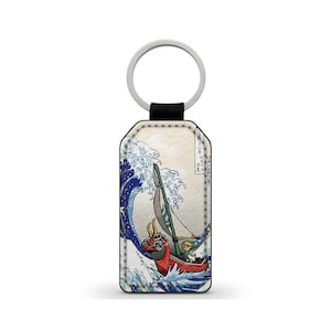 Peut inclure: Un porte-clés en cuir avec une image stylisée de Link de The Legend of Zelda: The Wind Waker naviguant sur un bateau à travers une grande vague, inspiré de la célèbre estampe japonaise sur bois "La Grande Vague de Kanagawa".