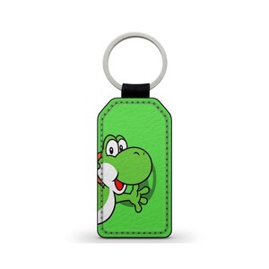 Op de afbeelding: Groene leren sleutelhanger met een gestikte rand met een Yoshi-cartoonfiguur dat uit het leer piept.