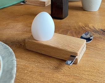 Puede incluir: Una mesa de madera con un jarrón de cristal marrón con flores secas, dos huevos blancos sobre hueveras de madera y una taza de cerámica.