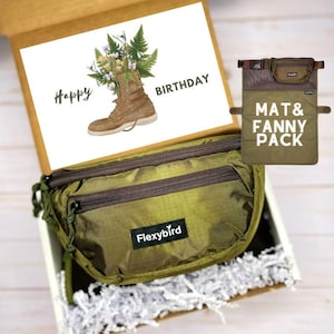 Op de afbeelding: Een groene heuptas met een bruine rits en de tekst "Flexybird" aan de voorkant. De heuptas zit in een cadeaudoos met wit geribbeld papier. Een kaart met de tekst "Happy Birthday" en een tekening van een laars met bloemen zit in de doos.