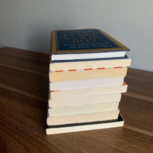 Pu&ograve; includere: Una pila di libri su una superficie di legno. Il libro in cima ha una copertina dorata con il titolo "Make Your Bed" e il testo "Little things that can change your life...and maybe the world."