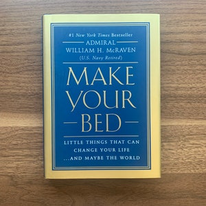 May include: A yellow and blue book cover with the title "Make Your Bed" by Admiral William H. McRaven (U.S. Navy Retired). The subtitle is "Little things that can change your life...and maybe the world."