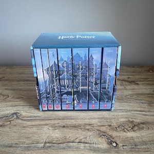 May include: A complete set of Harry Potter books in a box set. The books are arranged in a row, with a castle illustration on the spines. The box is blue with the title "Harry Potter: The Complete Series". The books are numbered 1 through 7.