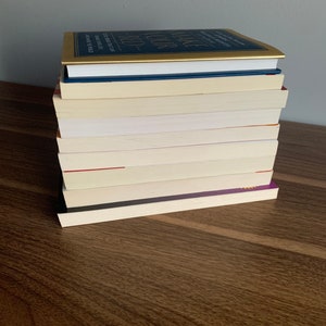 Pu&ograve; includere: Una pila di libri su una superficie di legno. Il libro in cima ha una copertina dorata con il titolo "Make Your Bed" in lettere nere. Gli altri libri hanno copertine bianche.