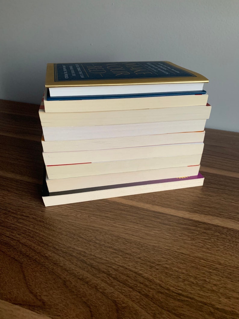 Pu&ograve; includere: Una pila di libri su una superficie di legno. Il libro in cima ha una copertina dorata con il titolo "Make Your Bed" in lettere nere. Gli altri libri hanno copertine bianche.