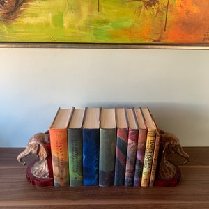 May include: A collection of Harry Potter books, with colorful spines, arranged between two decorative elephant bookends. The bookends are red and gold, and the books are various colors.