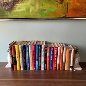 May include: A bookshelf filled with various books, including "Good to Great", "Think Again", "Unshakeable", "Made to Stick", "The Lean Startup", "The Startup Way", "The Subtle Art of Not Giving a F*ck", "The Compound Effect", and "Atomic Habits".