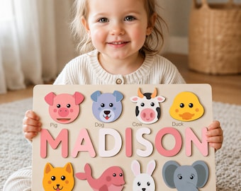 May include: A rectangular wooden puzzle board featuring the name MADISON in large pink and white letters. The board includes eight colorful animal cutouts: a pig, dog, cow, duck, cat, whale, rabbit, and elephant, each labeled with its name.