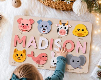 Puede incluir: Un rompecabezas de madera con el nombre MADISON en letras grandes de color rosa y blanco, rodeado de figuras de animales coloridos que incluyen un cerdo, perro, vaca, pato, gato, ballena, conejo y elefante, cada uno con su nombre etiquetado.
