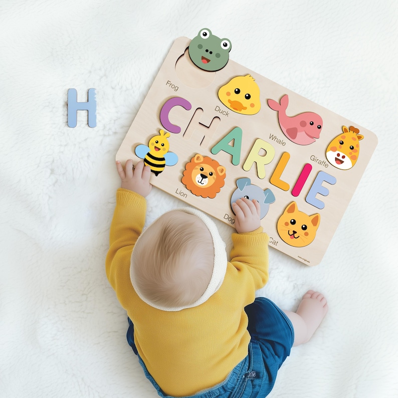 A baby is playing with a wooden puzzle featuring animal faces and the name "CHARLIE" written on it.