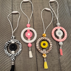 May include: Four car air fresheners with different animal print designs and flower accents. Each air freshener has a tassel hanging from the bottom.