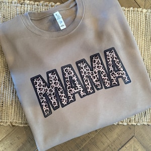 May include: A brown sweatshirt with the word "MAMA" printed in black with a leopard print design.