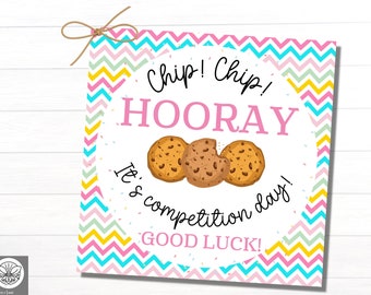 May include: A pink and blue chevron patterned card with a circle in the center. The circle has a pink background with the text "Chip! Chip! HOORAY It's competition day! GOOD LUCK!" and three chocolate chip cookies.