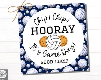 May include: Square volleyball-themed gift tag with a navy blue background covered in volleyballs. A white circle in the center has the words "Chip! Chip! Hooray! It's Game Day! Good Luck!" with a volleyball and two cookies.