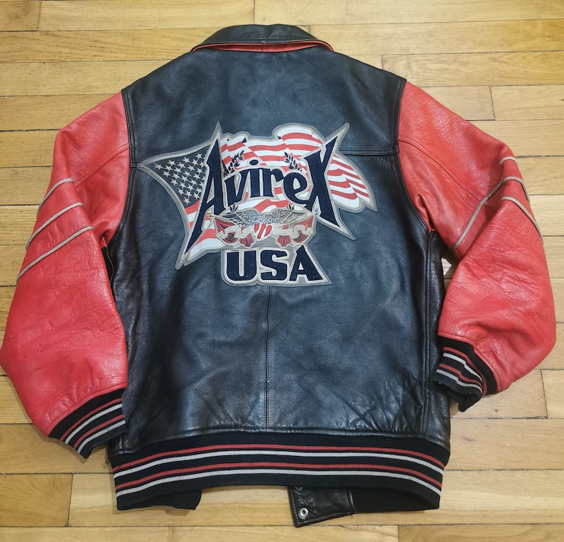 May include: A black and red leather varsity jacket with a large "Avirex USA" patch on the back. The patch features a stylised American flag and an eagle.