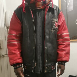 May include: A black leather varsity jacket with red sleeves and a white and silver stripe detail. The jacket has a zipper closure and a patch on the left side that says "USA Aviator".