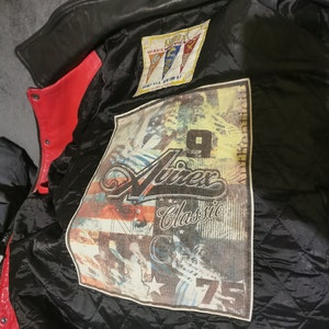 May include: A black leather jacket with a red lining. The jacket has a patch on the inside with the text "Ninex Classic" and a graphic of a motorcycle. The patch also has the text "New York City" and a star.
